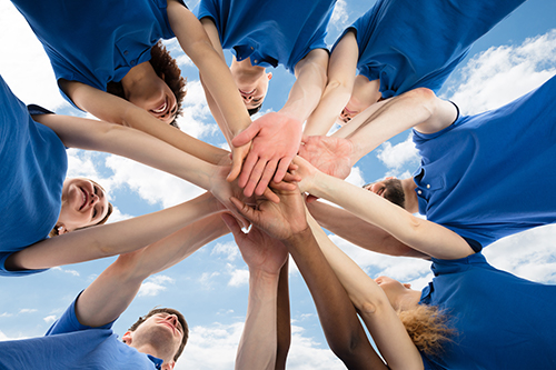 About Us team members standing in a circle with hands together.
